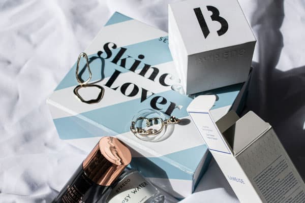 Envase abierto y cerrado de cosméticos blancos con impresión negra y rayas azules